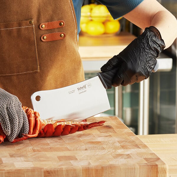 A person in black gloves using a Schraf cleaver to cut a lobster tail on a wooden surface.