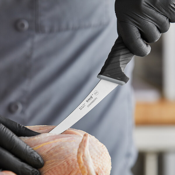 A hand in a black glove holding a Schraf curved boning knife cutting meat.