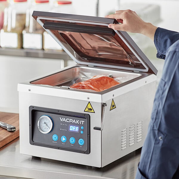 A person using a VacPak-It chamber vacuum packing machine to seal meat on a counter.