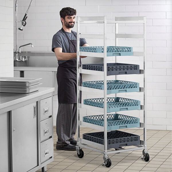 A man standing in a professional kitchen next to a Steelton aluminum glass rack cart.