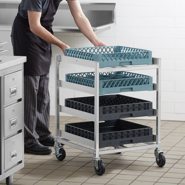 A man in a black apron pushing a Regency aluminum glass rack cart with blue baskets.