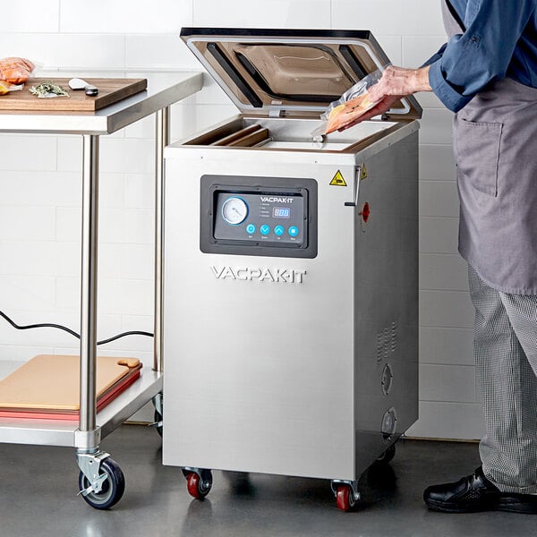 A man using a VacPak-It floor model chamber vacuum sealer on a table.