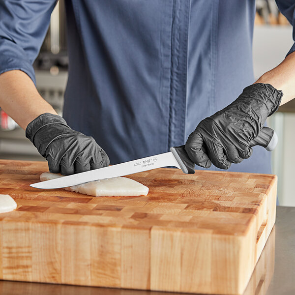 A person using a Schraf fillet knife to cut meat on a cutting board.