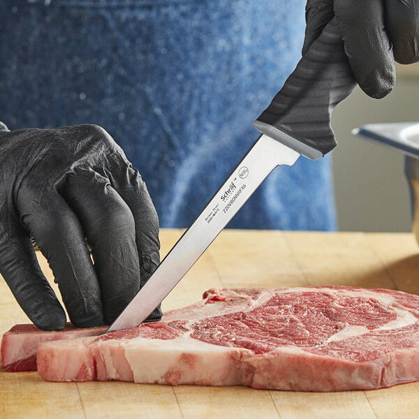 A person in black gloves using a Schraf narrow boning knife to cut meat on a table.