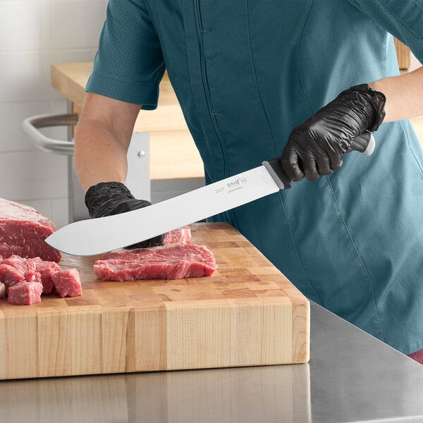 A person using a Schraf butcher knife to cut raw meat on a cutting board.