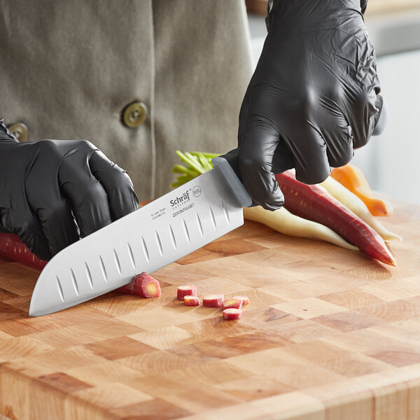 A person in black gloves uses a Schraf Santoku knife to cut peppers on a cutting board.