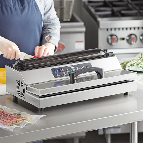A woman using a VacPak-It Ultima vacuum packing machine on a counter in a professional kitchen.