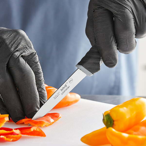 A hand in a black glove using a Schraf paring knife to cut a yellow bell pepper.