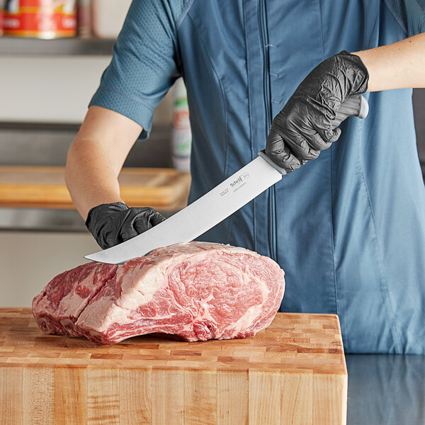 A person using a Schraf Cimeter knife to cut raw meat on a wooden surface.