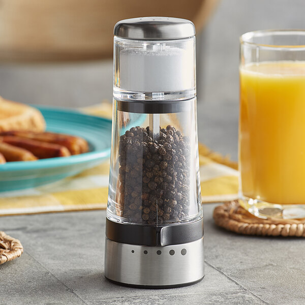 An OXO pepper grinder on a counter next to a plate of food with a glass of orange juice.