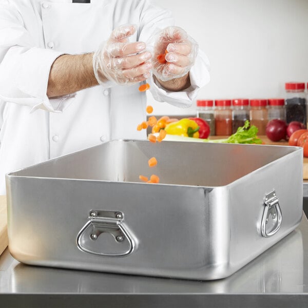 A chef pouring carrots into a Vollrath aluminum roasting pan.