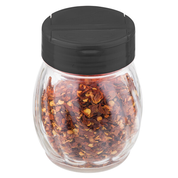 A Tablecraft clear plastic shaker with a black flip top lid on a counter filled with red pepper flakes.
