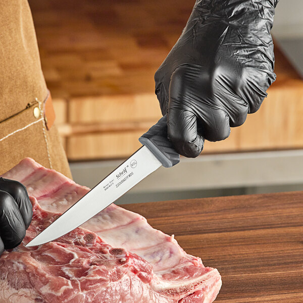 A person in black gloves using a Schraf boning knife to cut meat on a cutting board.