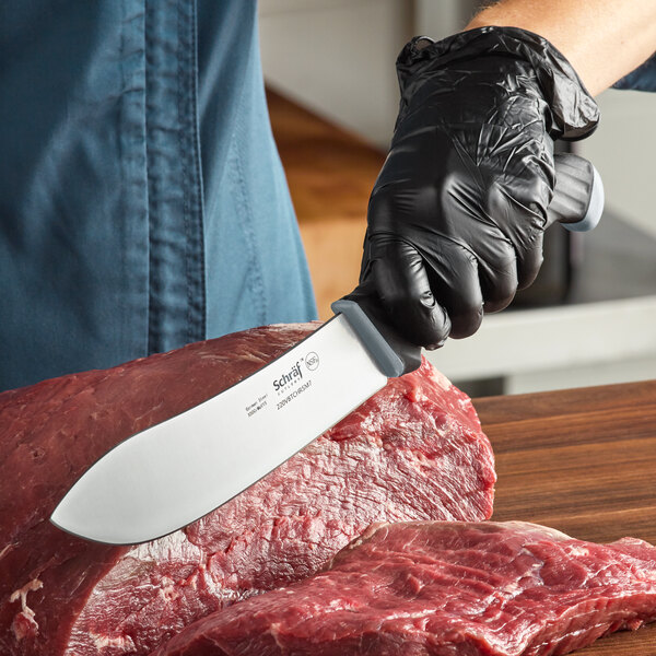 A person in black gloves uses a Schraf butcher knife to cut a piece of meat.