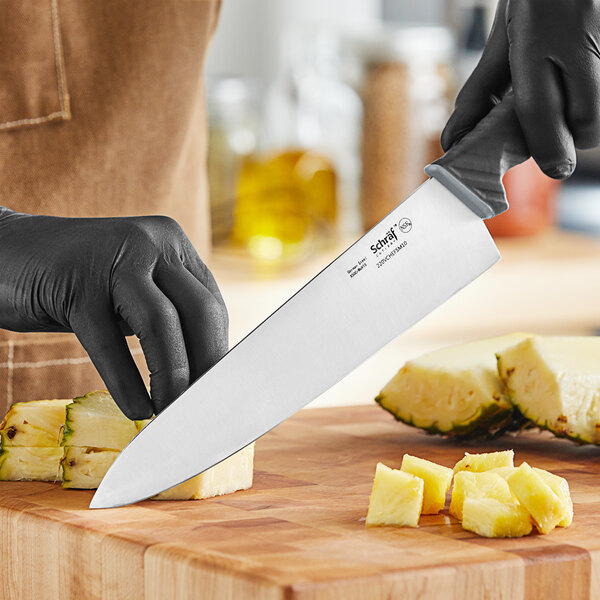 A person in black gloves uses a Schraf chef knife to cut a pineapple.