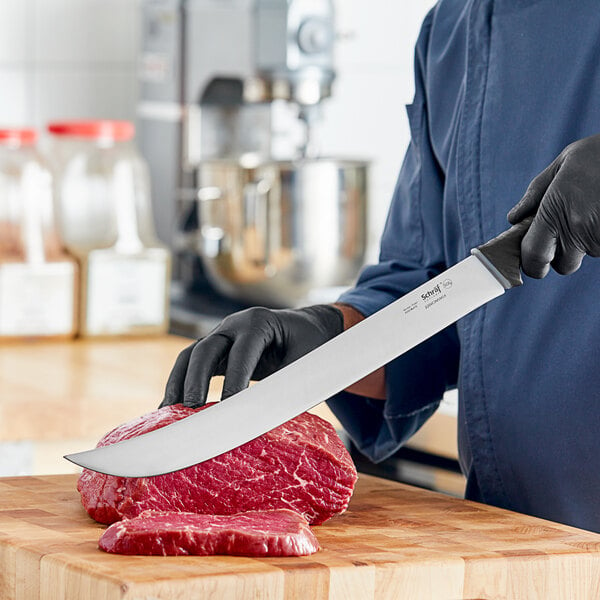 A man in a black glove using a Schraf Cimeter knife to cut meat on a cutting board.