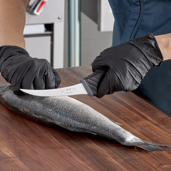 A person in a black glove using a Schraf curved boning knife to cut a fish.