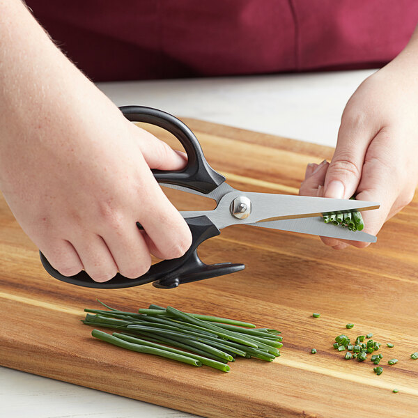 A hand using Mercer Culinary Japanese steel kitchen scissors to cut green onions on a cutting board.