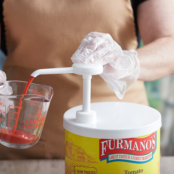 A person using a Tablecraft condiment pump to pour tomato sauce into a measuring cup.