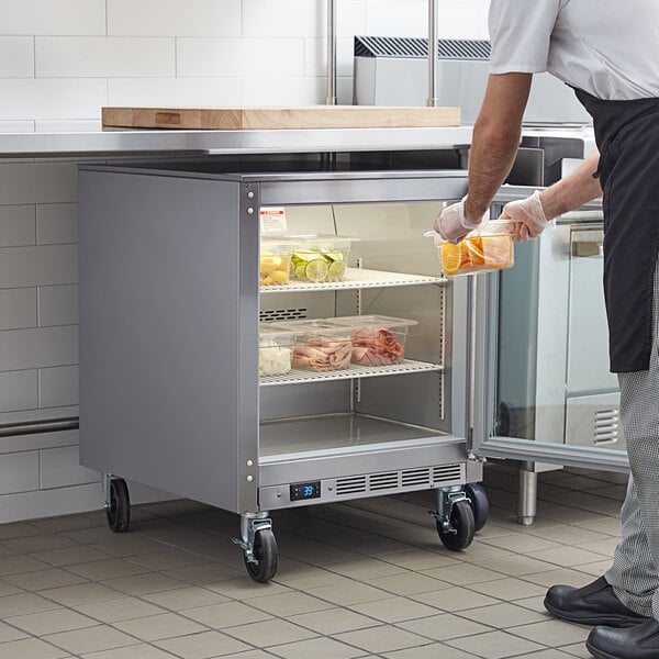 A man in a school kitchen putting food into a Beverage-Air undercounter refrigerator.