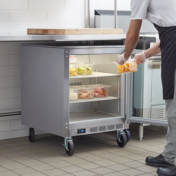 A man in a school kitchen putting food into a Beverage-Air undercounter freezer.