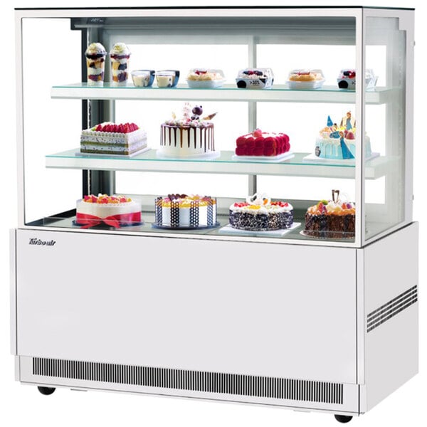 A Turbo Air white refrigerated bakery display case with three tiers of cakes and desserts.
