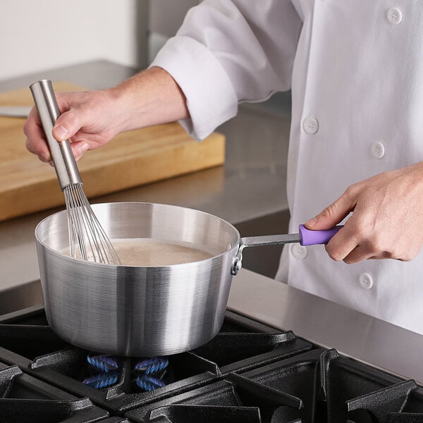 A person stirring food in a Choice aluminum sauce pan on a stove.