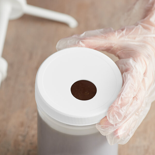 A person in gloves using a Tablecraft threaded adapter lid to pump liquid into a white container.