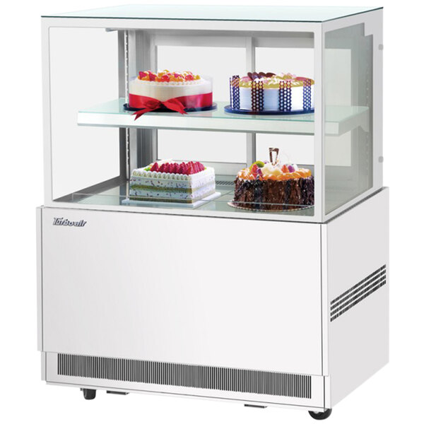 A Turbo Air white refrigerated bakery display case with cakes on it.