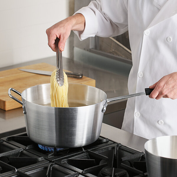 A chef in a white coat stirring food in a Choice aluminum sauce pan on a stove.