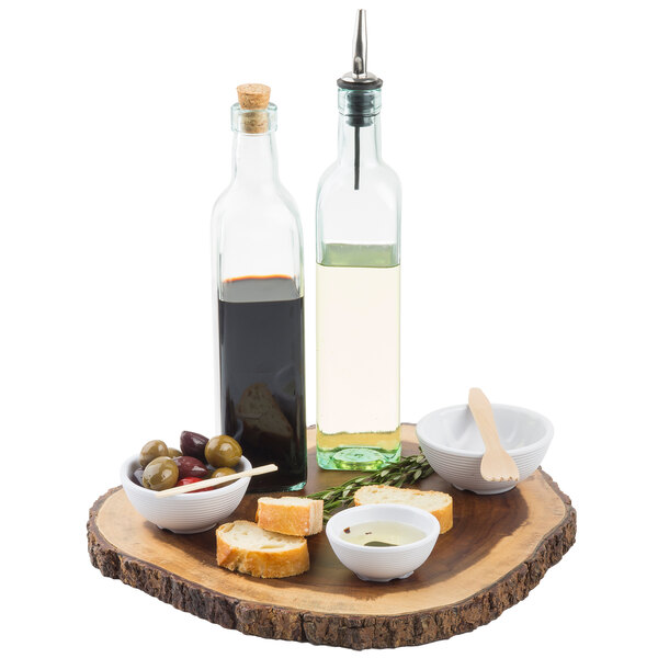 A Tablecraft green glass oil and vinegar bottle on a wood platter with olives, bread and olive oil.