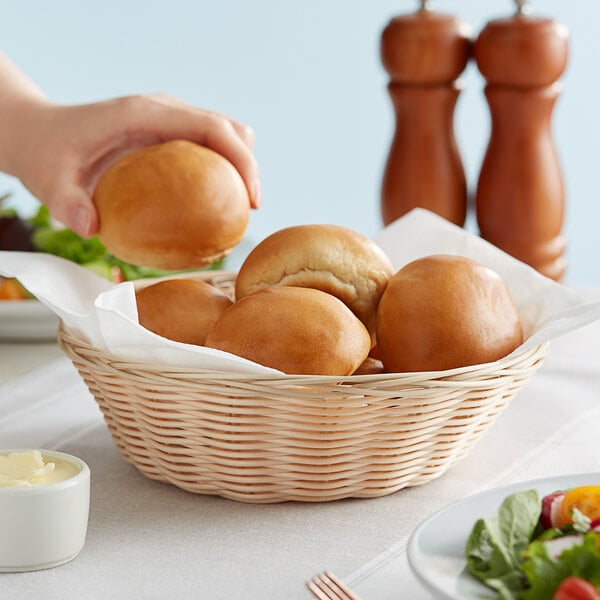 A hand putting a bun into a Tablecraft natural-colored polypropylene and steel bread basket.