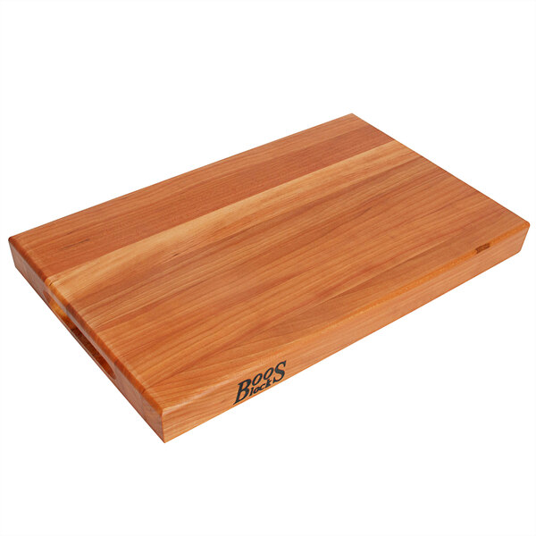 A John Boos cherry wood cutting board with hand grips on a table.
