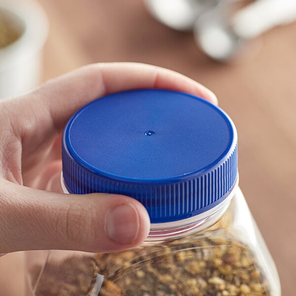 A hand holding a plastic container with a blue flat top induction-lined spice lid.