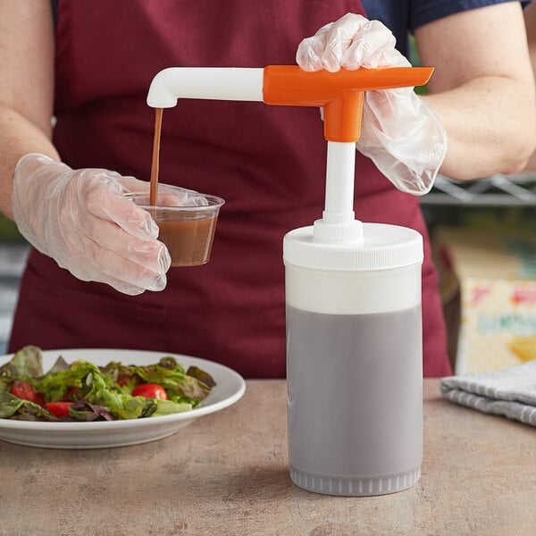 A person using a Tablecraft condiment pump to pour brown liquid into a plastic container.