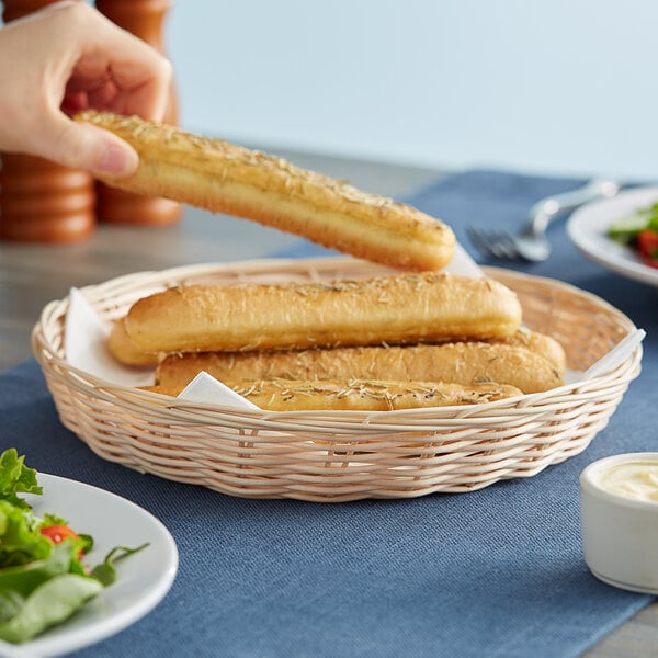A person holding a Tablecraft natural-colored round bread basket with bread sticks.