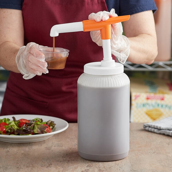 A woman using a Tablecraft WideMouth Pelican Pump to pour brown liquid into a white container.