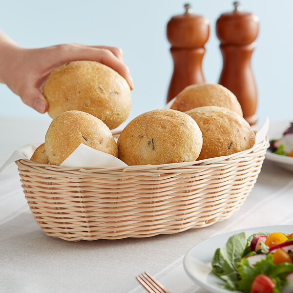 A hand holding a Tablecraft oval natural-colored polypropylene basket of bread