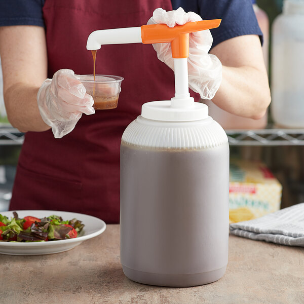 A person using a Tablecraft condiment pump to pour brown liquid into a white plastic container.