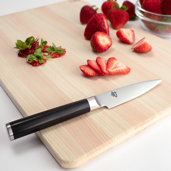 A Shun Classic paring knife with a black pakkawood handle on a cutting board with strawberries.