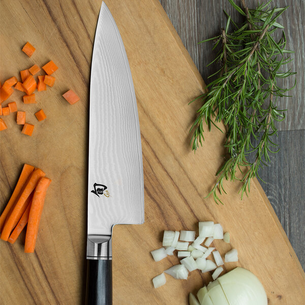 A Shun Classic cook's knife on a cutting board with carrots, onions, and other vegetables.