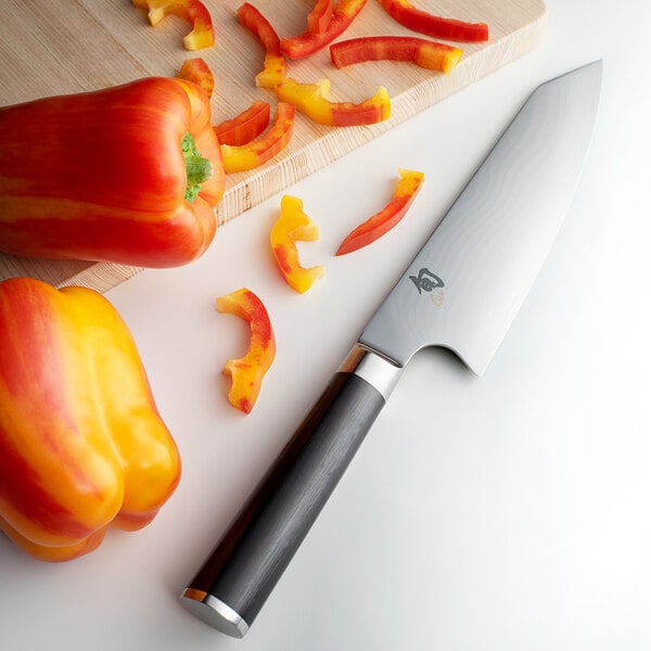 A Shun Classic Kiritsuke knife next to sliced yellow, orange, and red bell peppers.