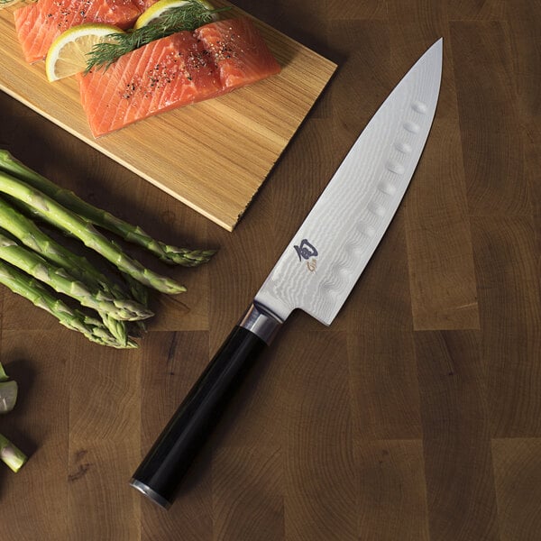 A Shun Classic Chef Knife next to a cutting board and asparagus.