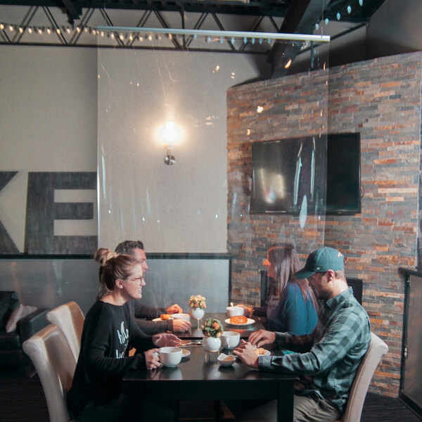 A group of people sitting at a table in a restaurant with a clear PVC partition hanging above them.