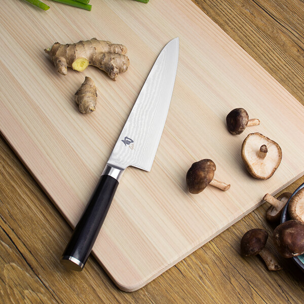 A Shun Classic Asian cook's knife on a cutting board with mushrooms and other vegetables.