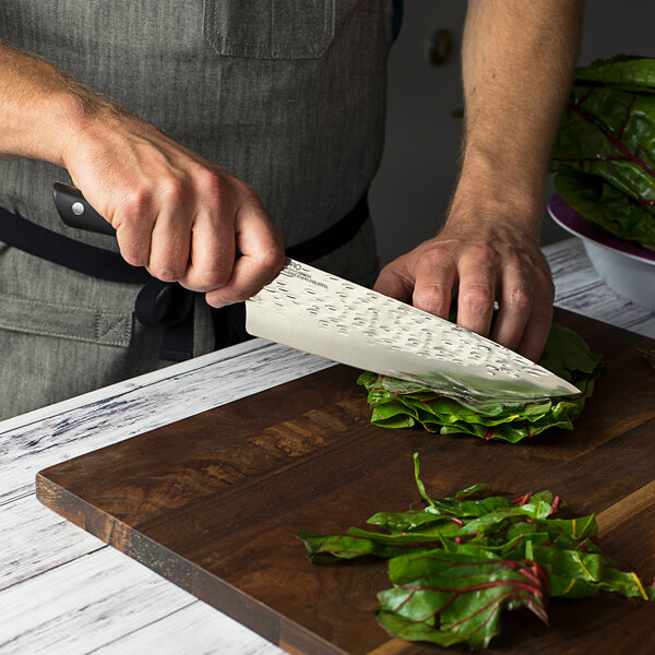 A person using a Kai PRO chef knife to cut vegetables on a cutting board.