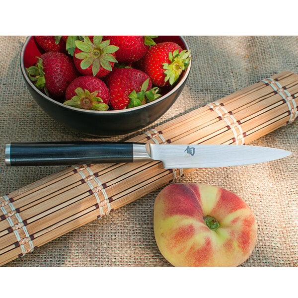 A Shun Classic paring knife cutting strawberries for a bowl of fruit.