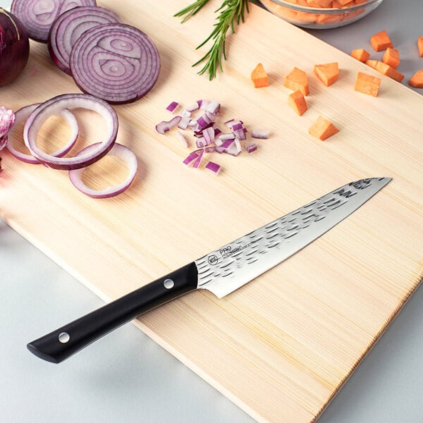 A Kai PRO utility knife on a cutting board with sliced onions and other vegetables.