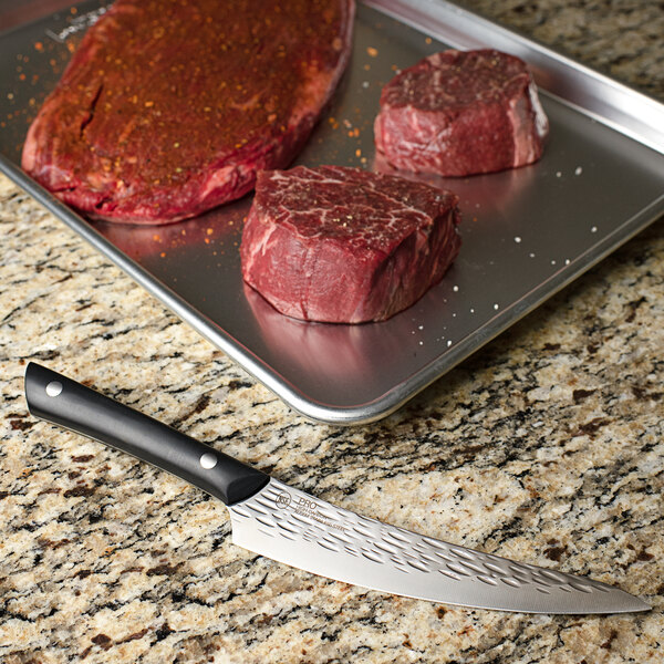 A Kai PRO curved boning and fillet knife next to a piece of raw meat on a tray.