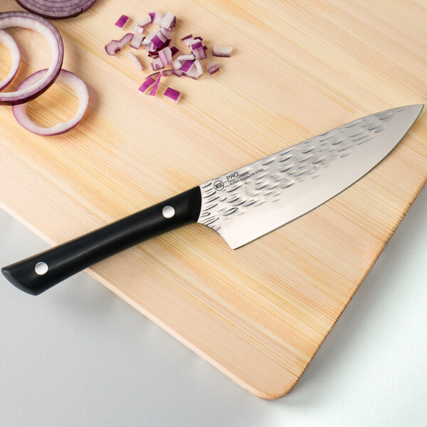 A Kai PRO chef knife on a cutting board with onions.